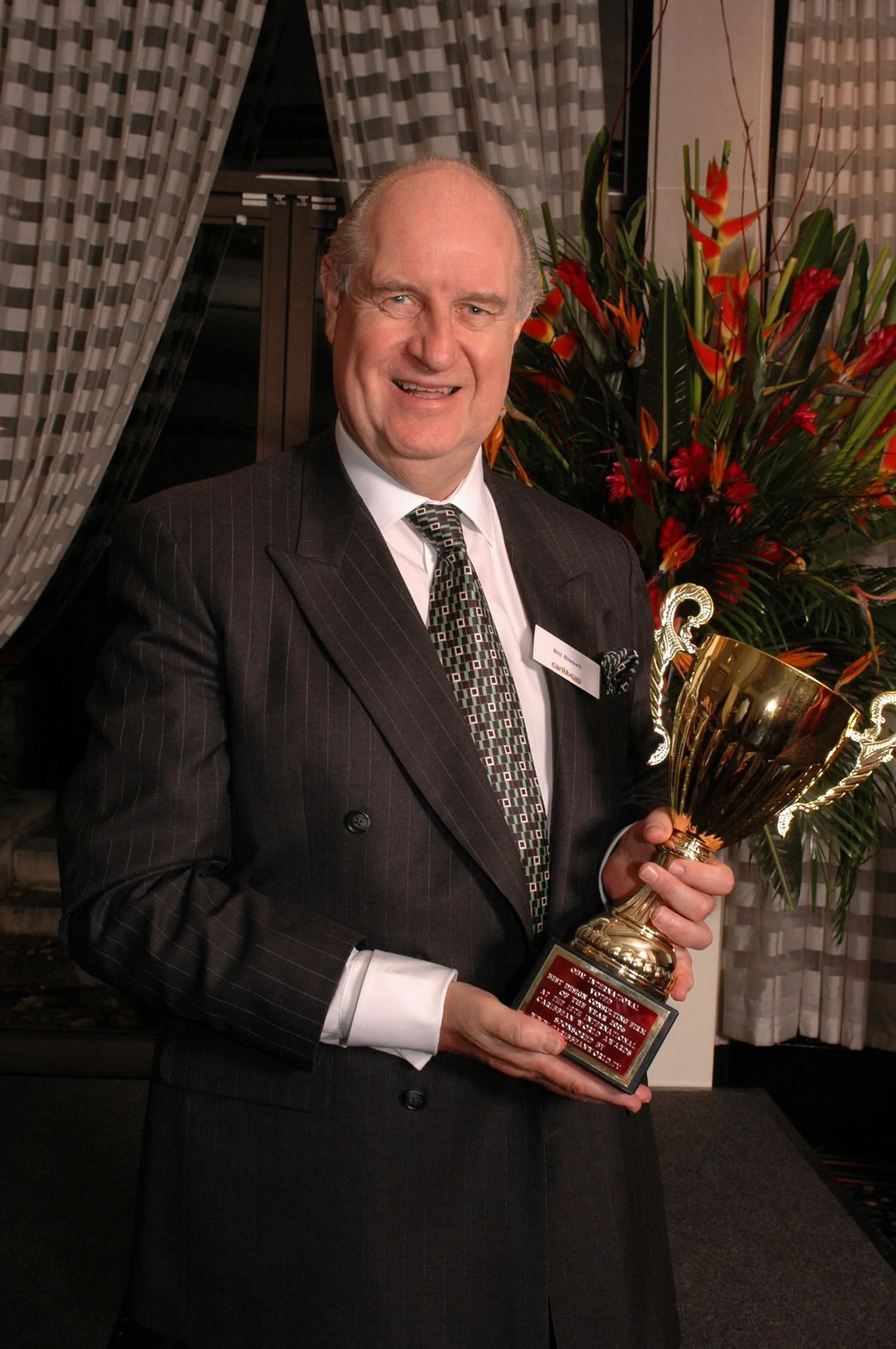 Bill Bissell in a pinstripe suit, smiling, holding the gold Caribbean World Awards cup