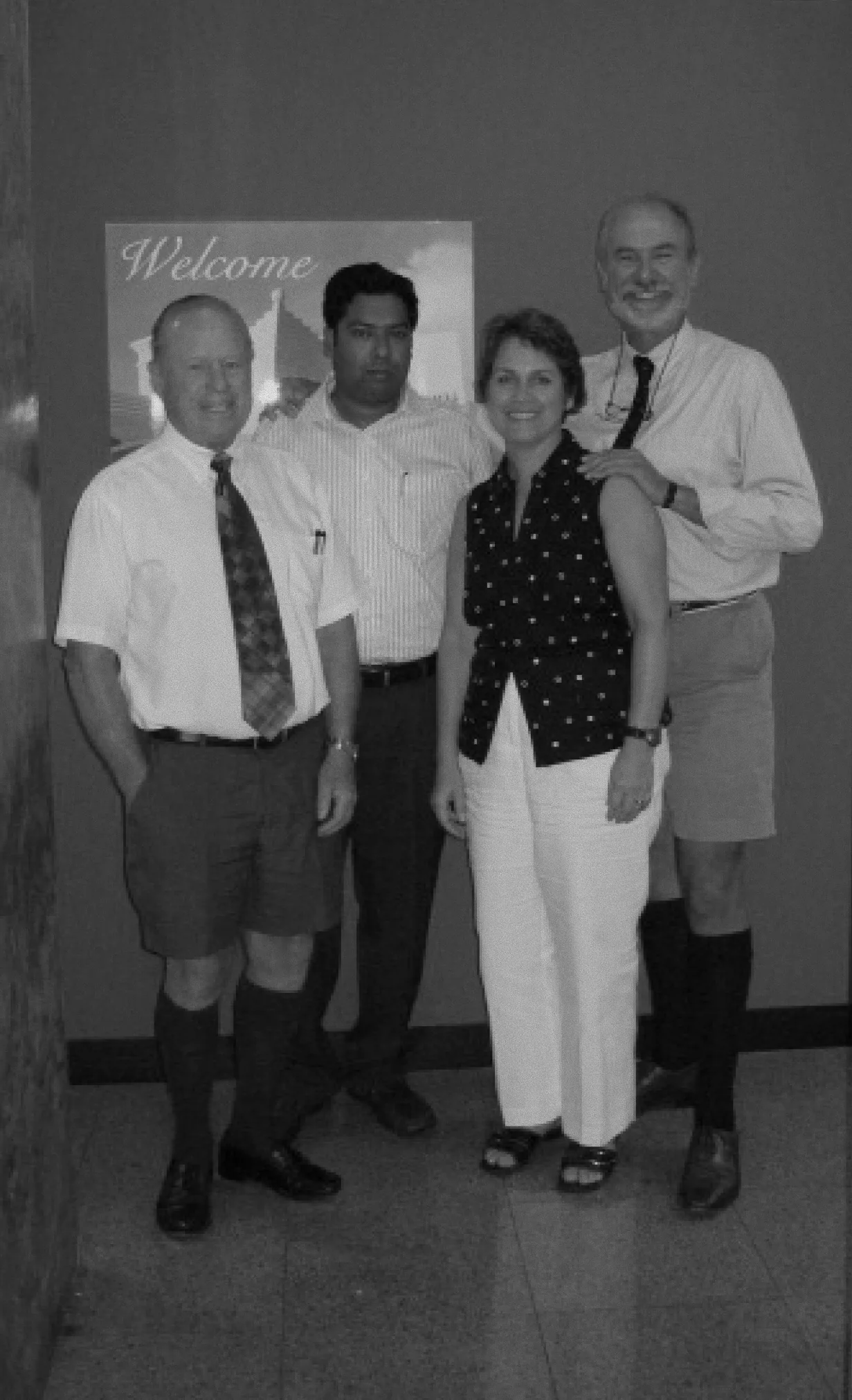 Four members of the BVI office in front of a Welcome poster, a black and white photograph