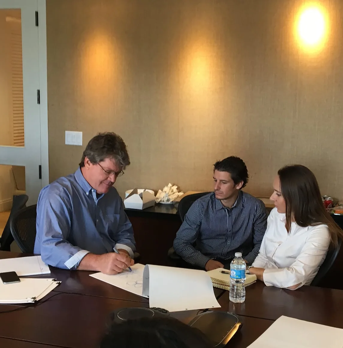 Doug Kulig sketching at a meeting table while two colleagues watch