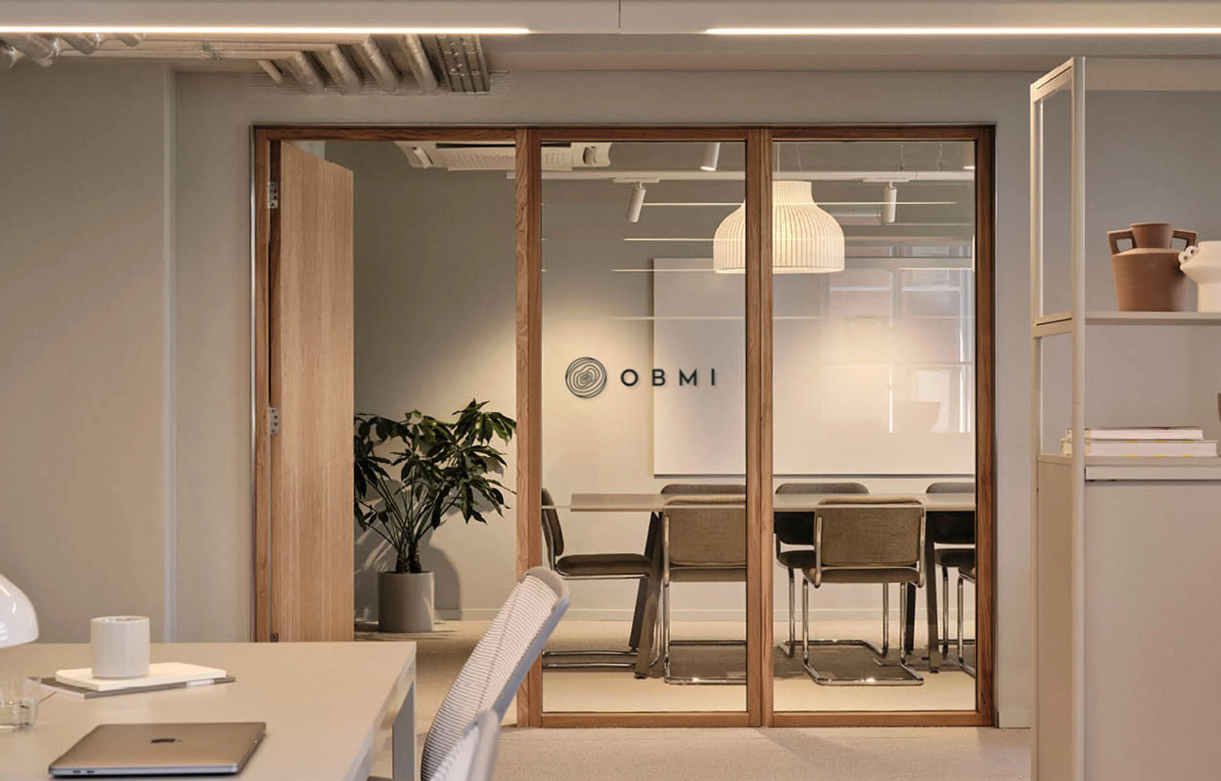 The OBMI London office: a glazed meeting room with the OBMI mark on the door, warm timber and a long table