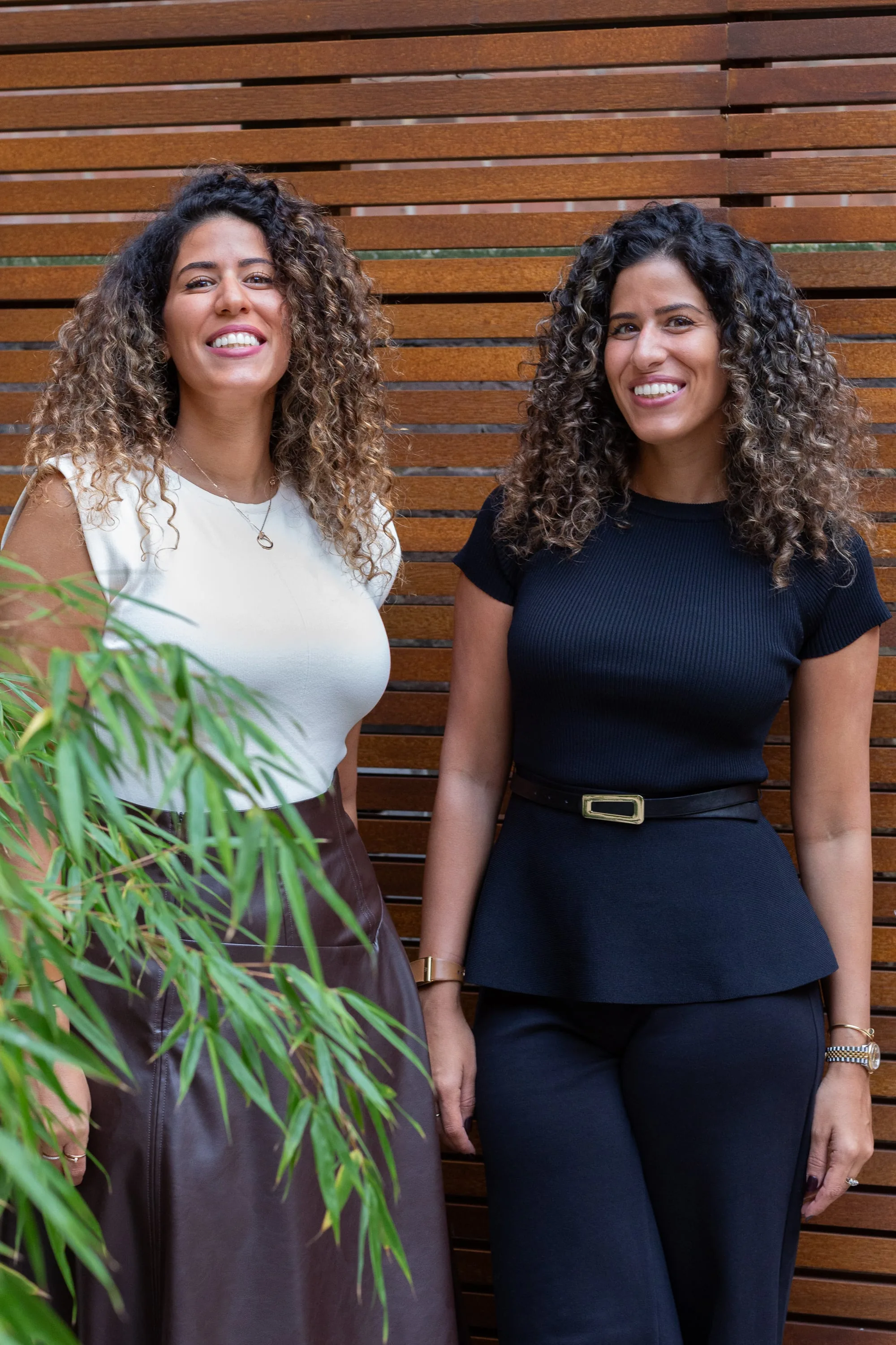 Nadeen and Shereen El Margoushy, laughing, against a slatted timber wall