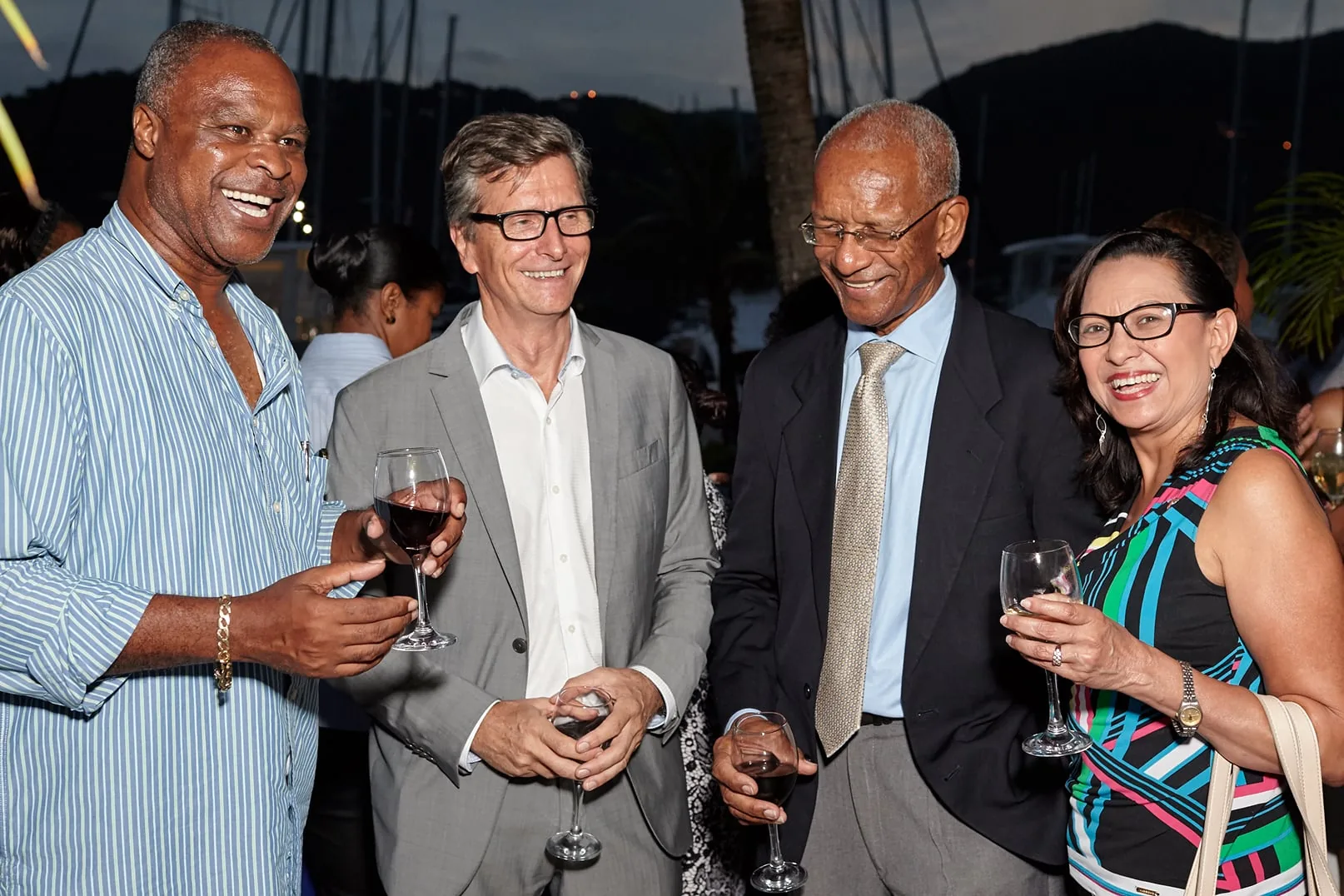 Four guests laughing with glasses of wine at the marina at dusk
