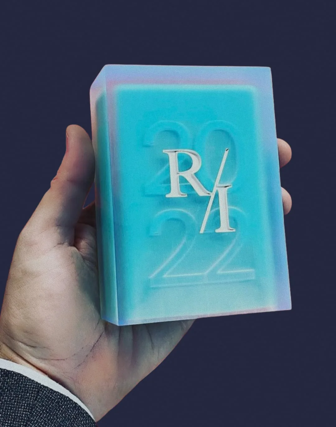 The 2022 Radical Innovation Award, a block of pale blue resin, held in a hand