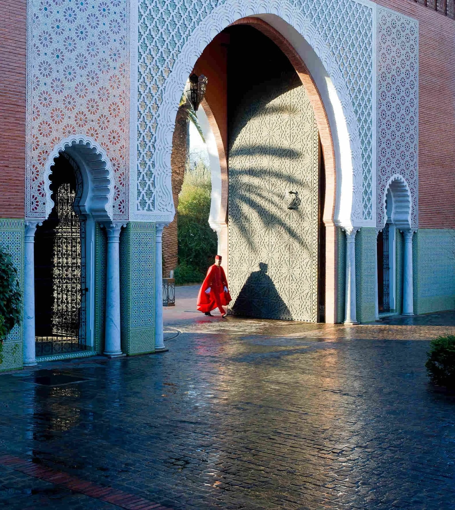 The entrance gate of Le Royal Mansour, Marrakech — zellige, carved plaster and a doorman in red