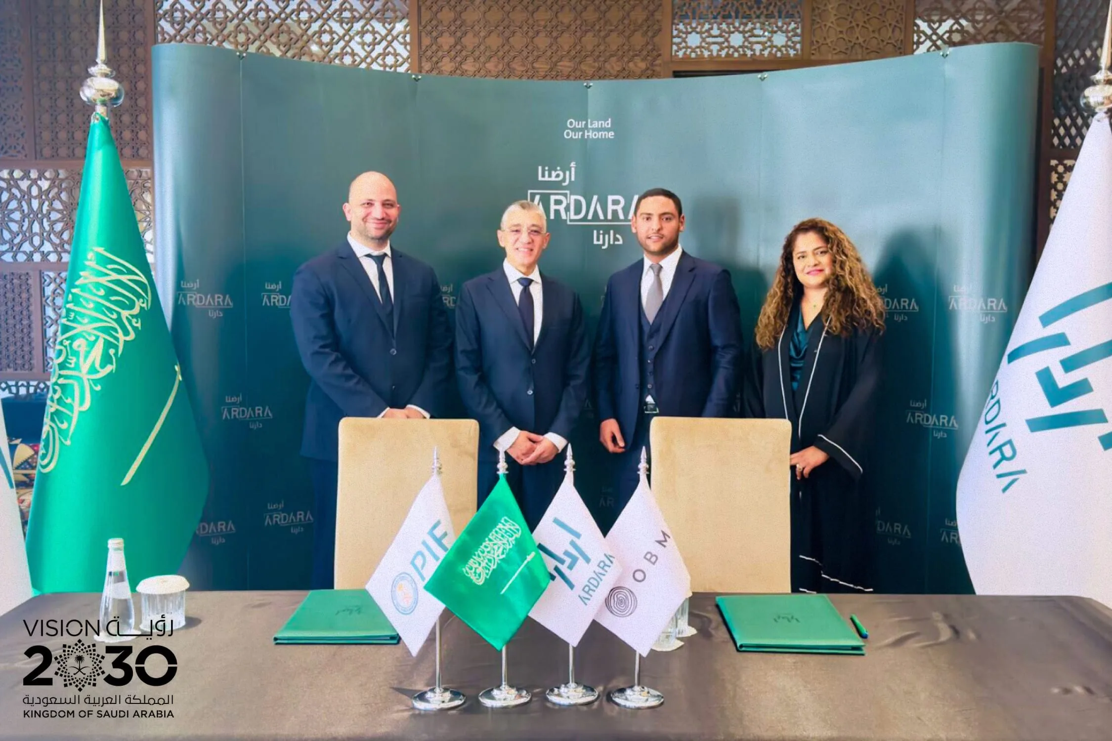 A signing ceremony, with the Saudi, PIF, Ardara and OBMI flags on the table