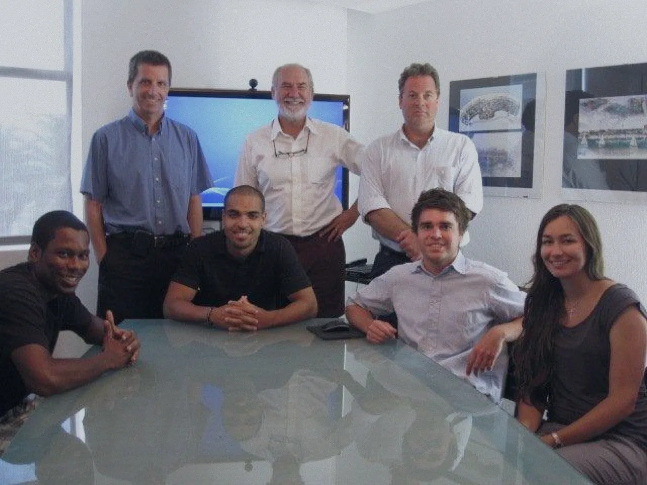 Seven members of the team around a glass table in the Miami office, renderings on the wall