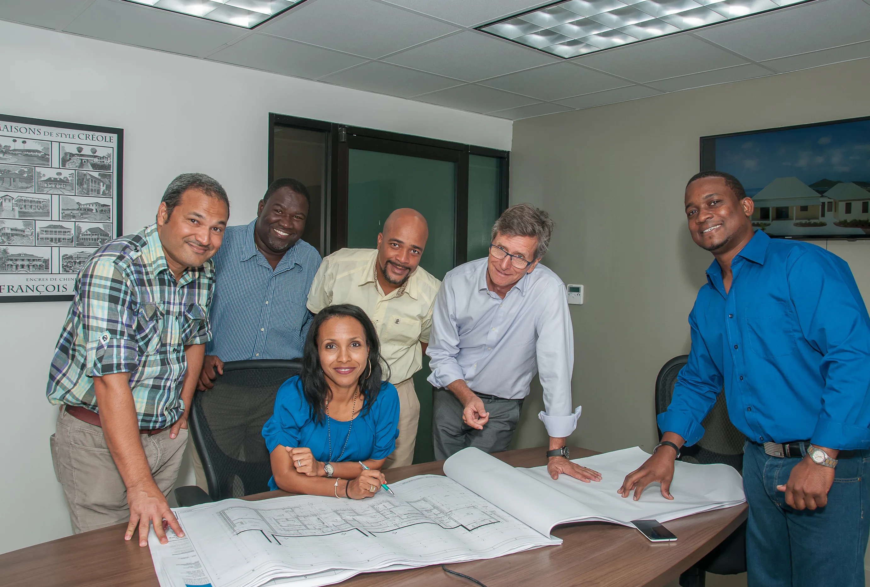 Six members of the team leaning over a set of blueprints in a meeting room