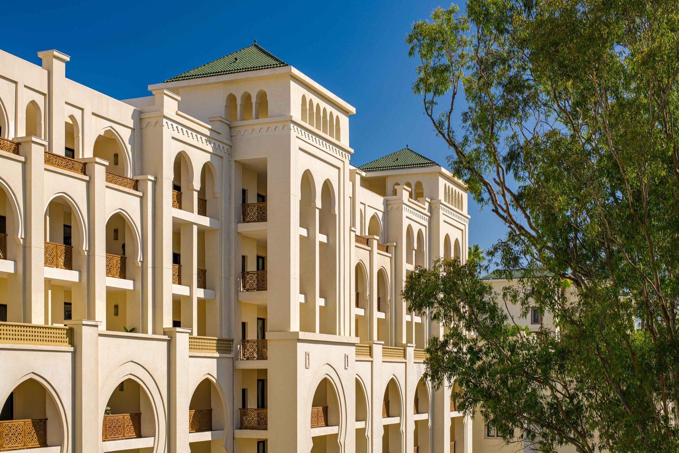 A new wing with arched balconies and green-tiled roofs beside a eucalyptus