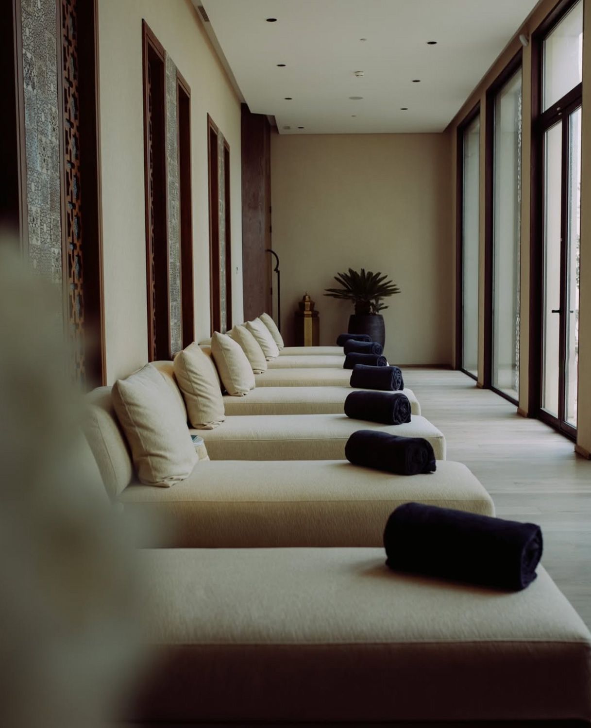 Spa loungers with rolled towels along a corridor of tall windows
