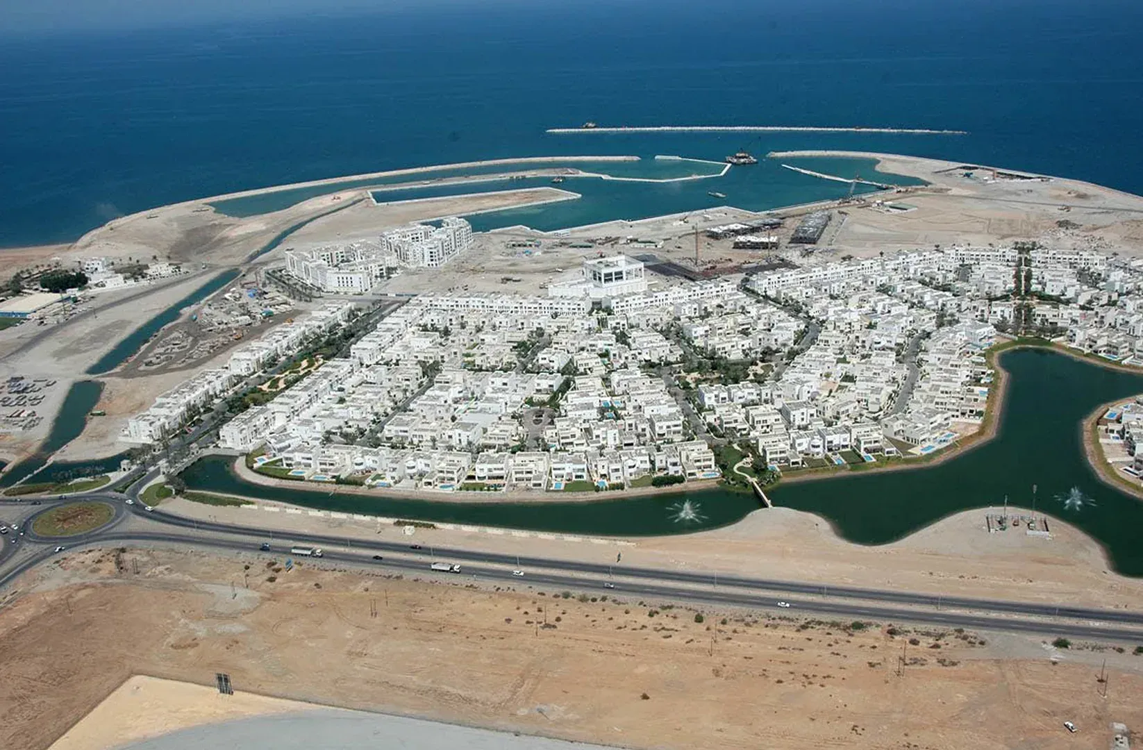 The community from the air: white houses between canals and lakes, the marina breakwater beyond