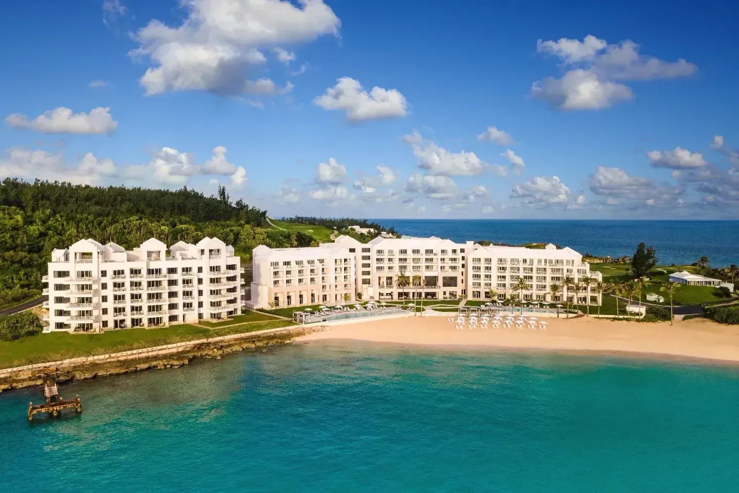 The hotel and residences from the sea, white gables above the beach, the golf course behind