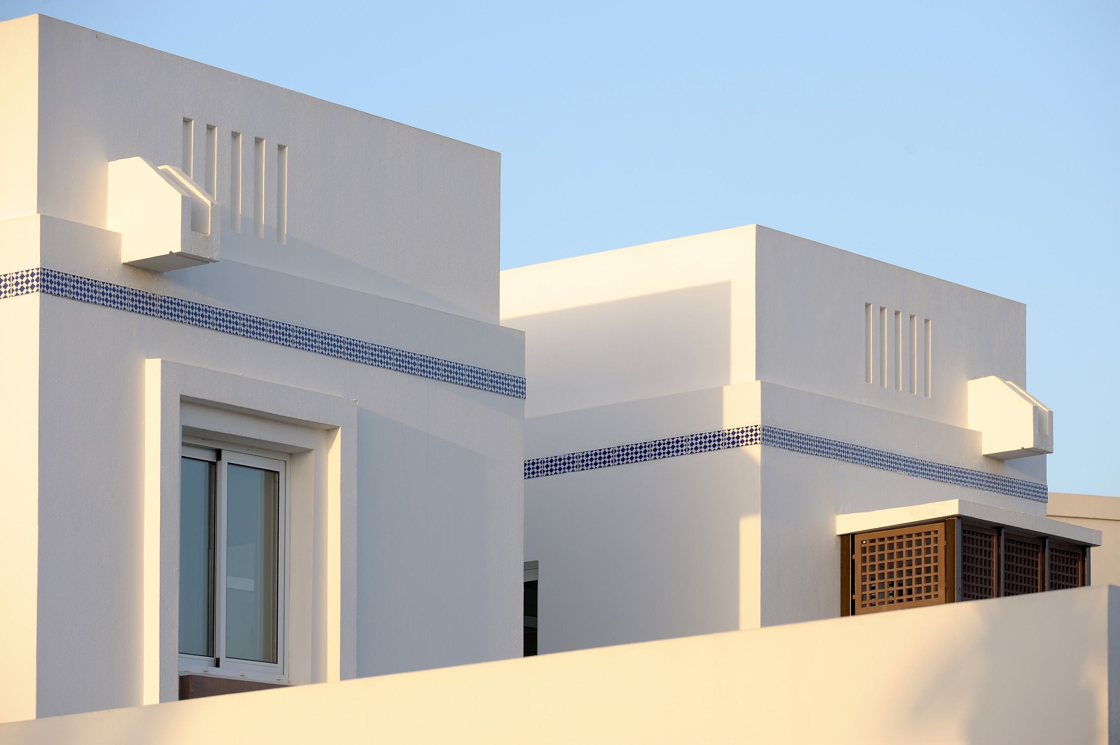 Rows of white houses with slatted balconies under a hard blue sky