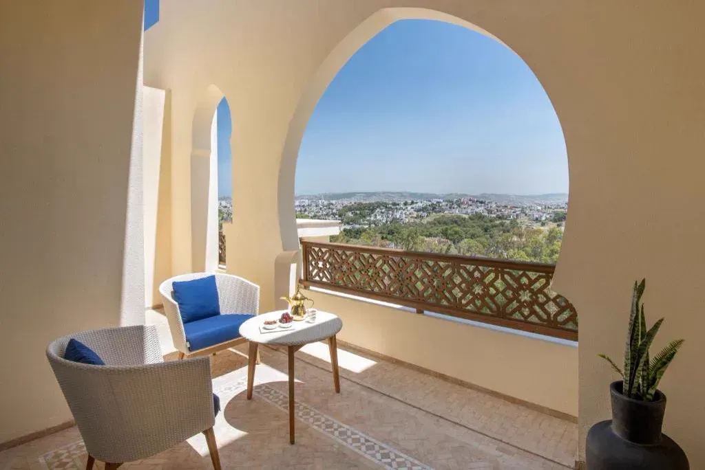 A terrace through a pointed arch, wicker chairs, Tangier and the hills beyond