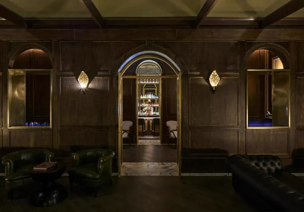 A dark panelled bar seen through a brass-framed arch, leather armchairs before it