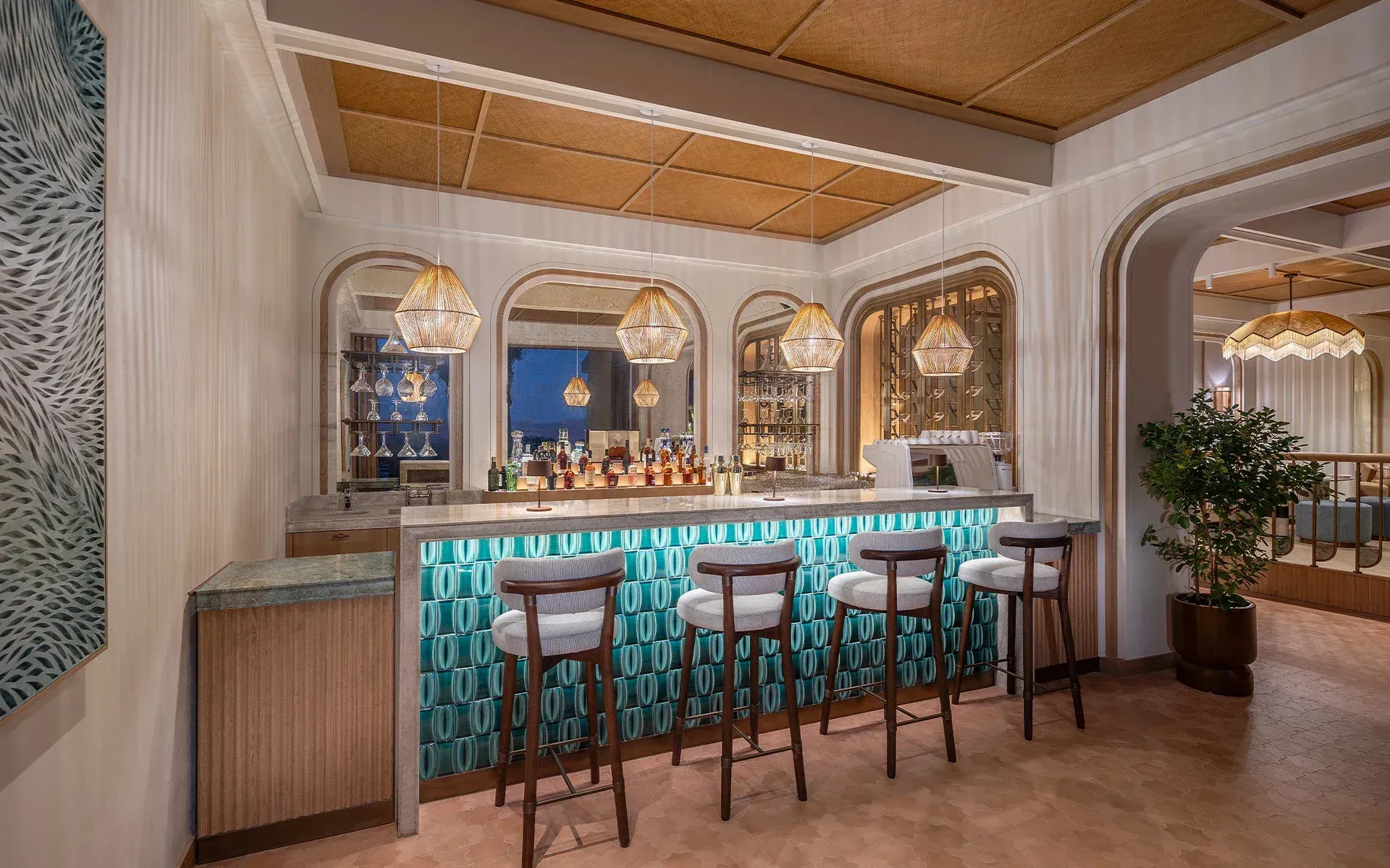 The bar at dusk: a turquoise-tiled counter, rope pendants, the sky in the arched mirrors