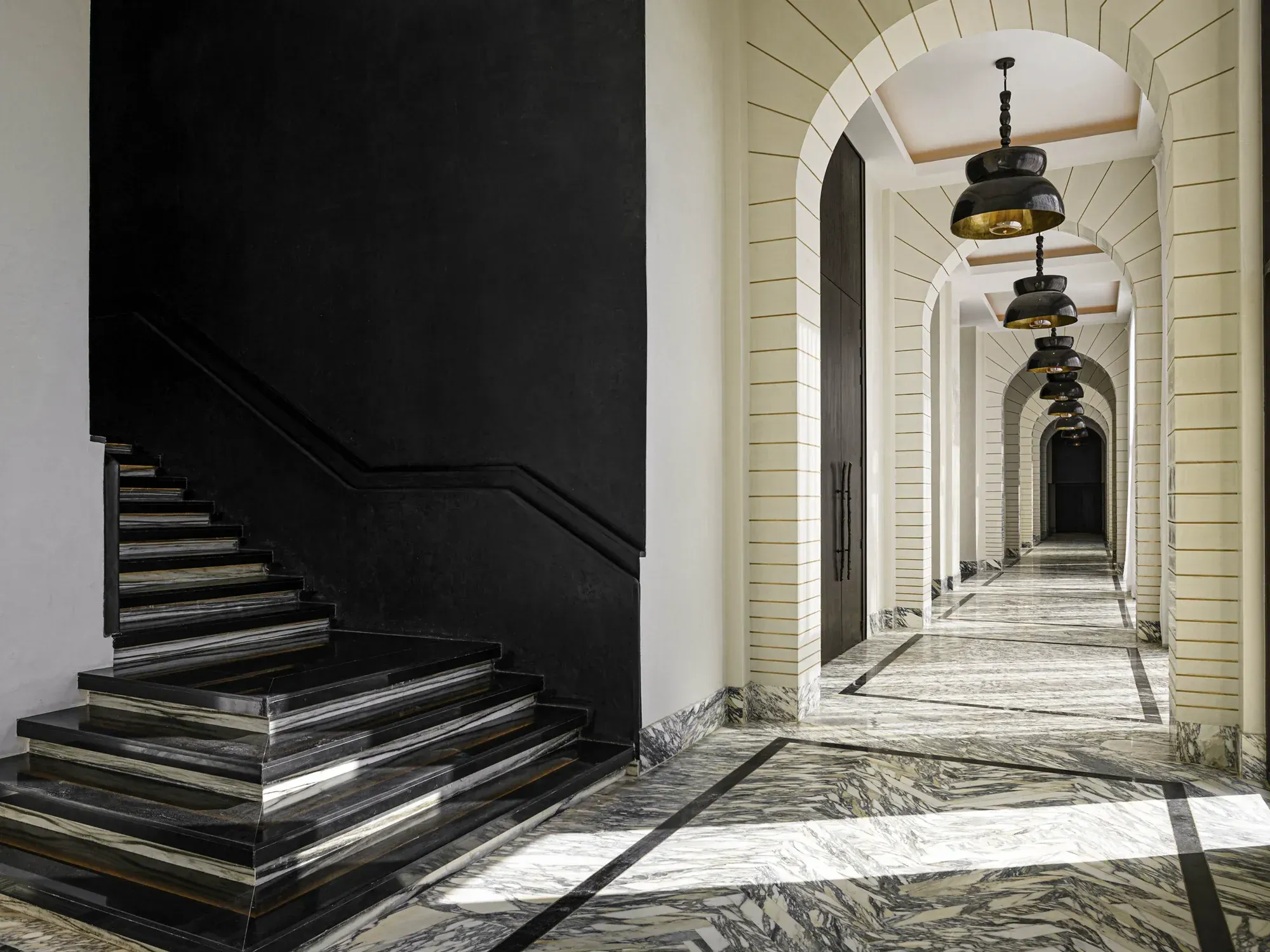 A black marble stair beside an arched corridor of pendant lamps