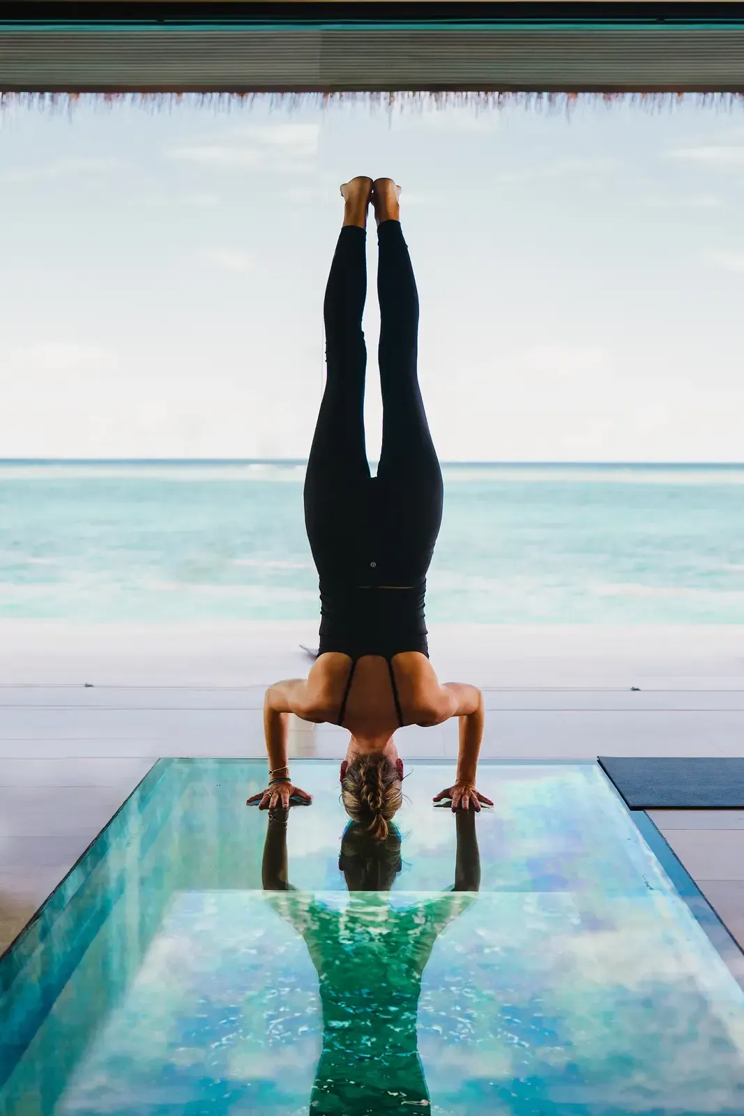 A figure in a headstand on a glass floor, the sea open behind