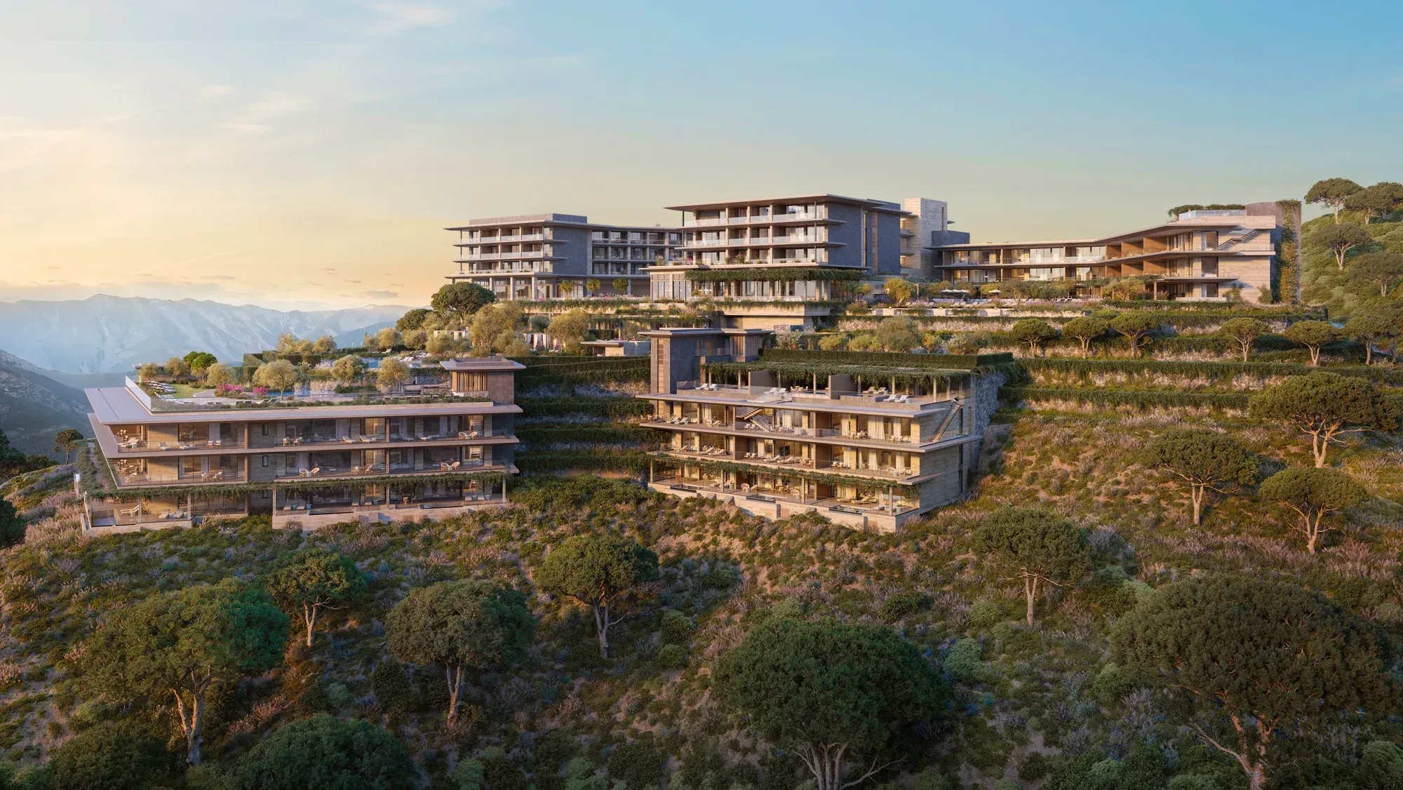 The resort stepping down a wooded hillside at dusk, mountains behind
