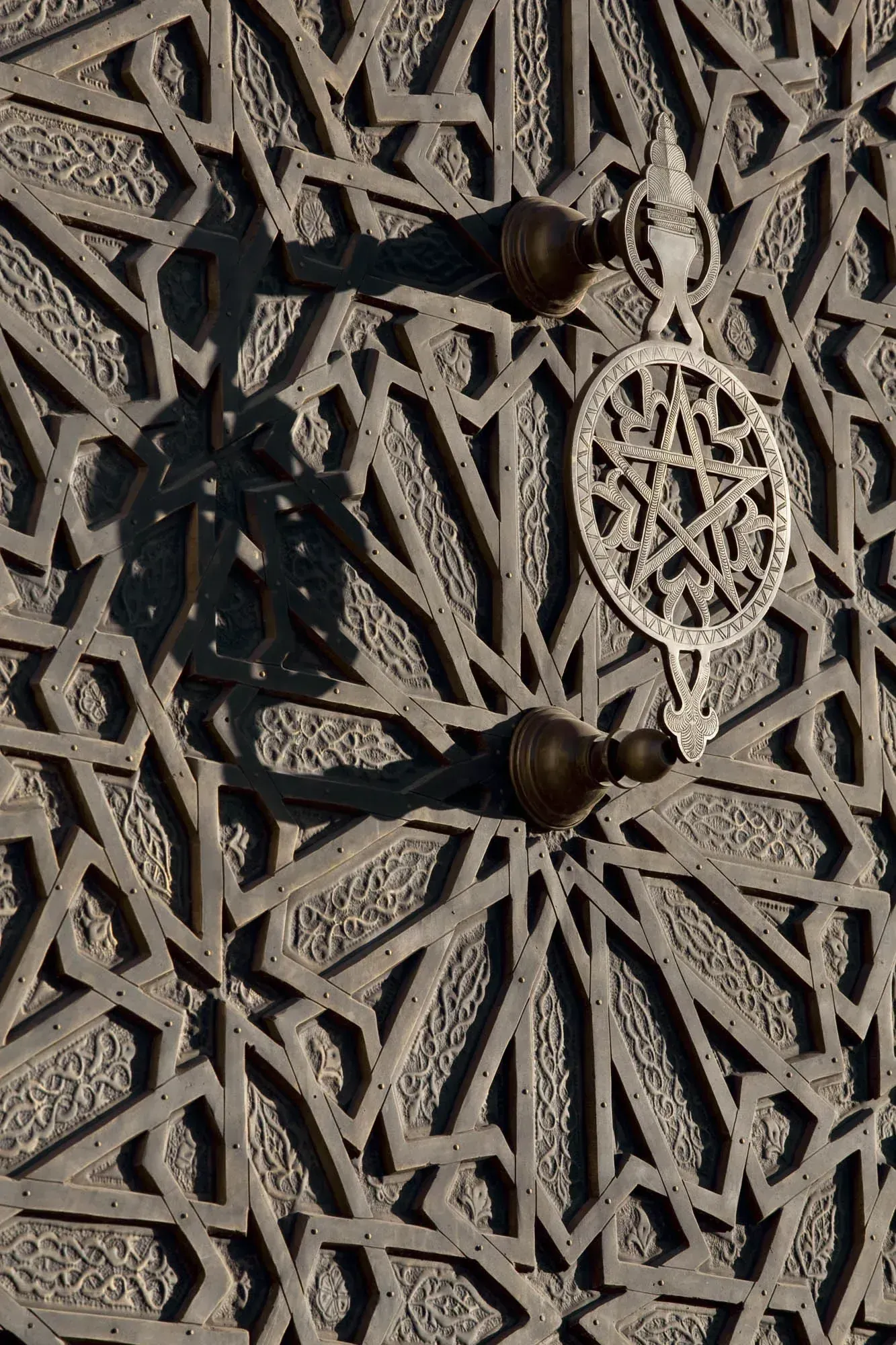 Etched bronze door with a star knocker, in low sun