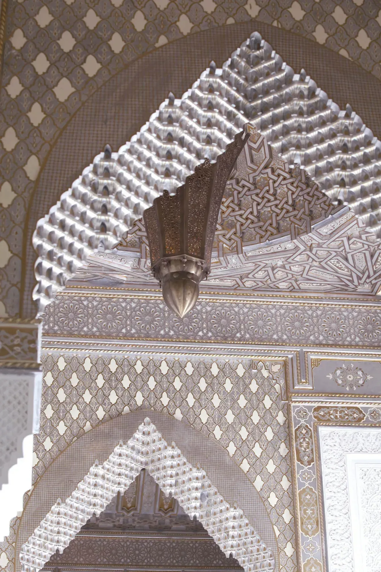 Carved muqarnas and a bronze lantern above an arch