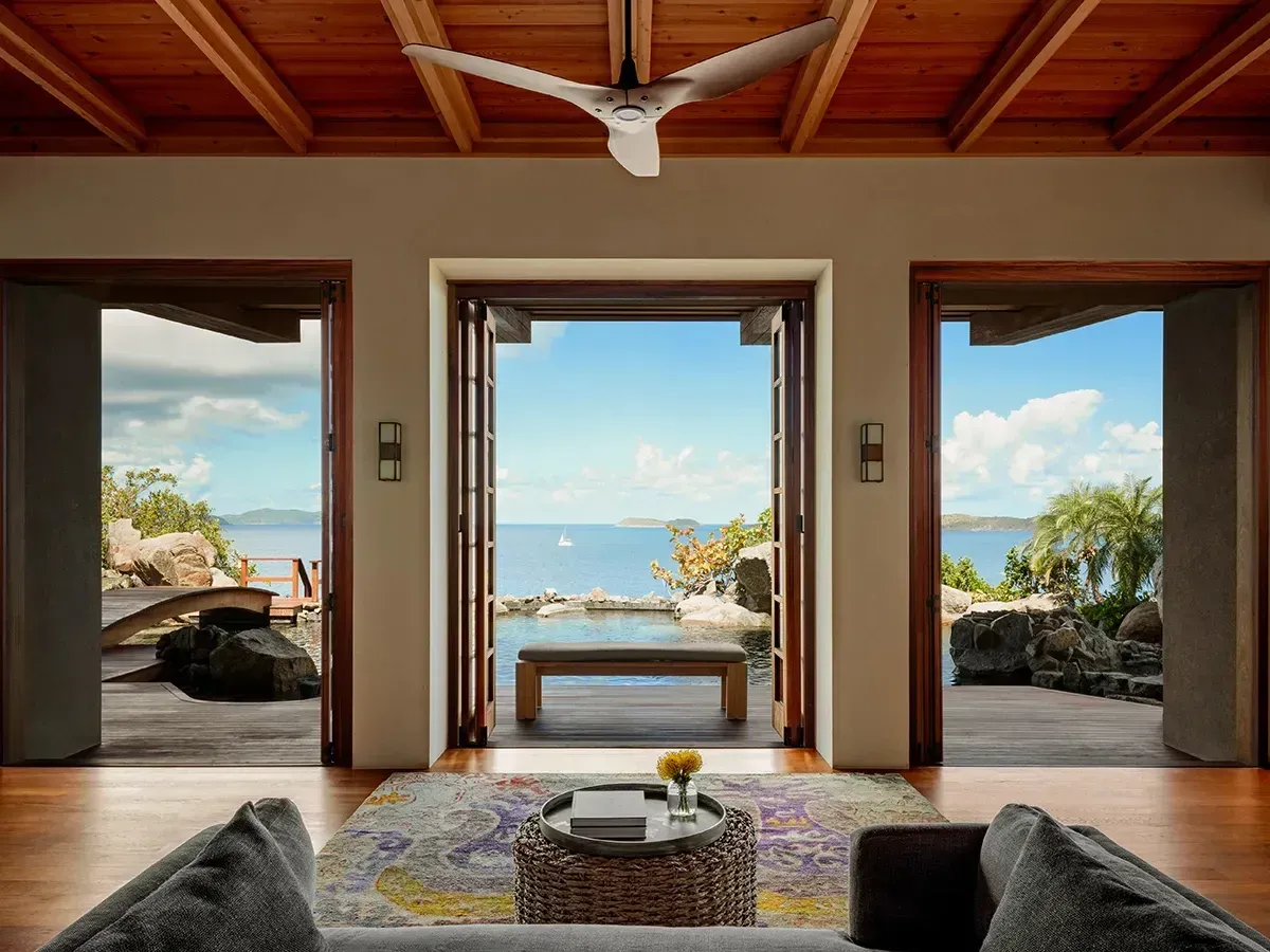 The living room under a timber ceiling, three doorways open to the pool and the channel