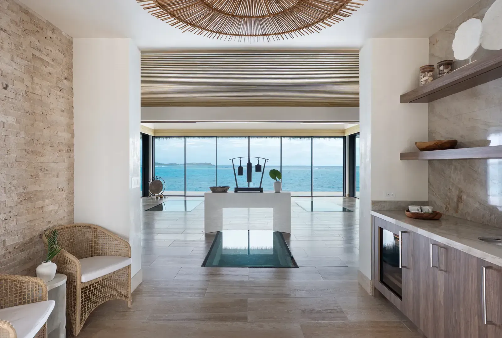 The lobby: a rattan pendant, a stone wall, the bar, a glass floor and the sea beyond