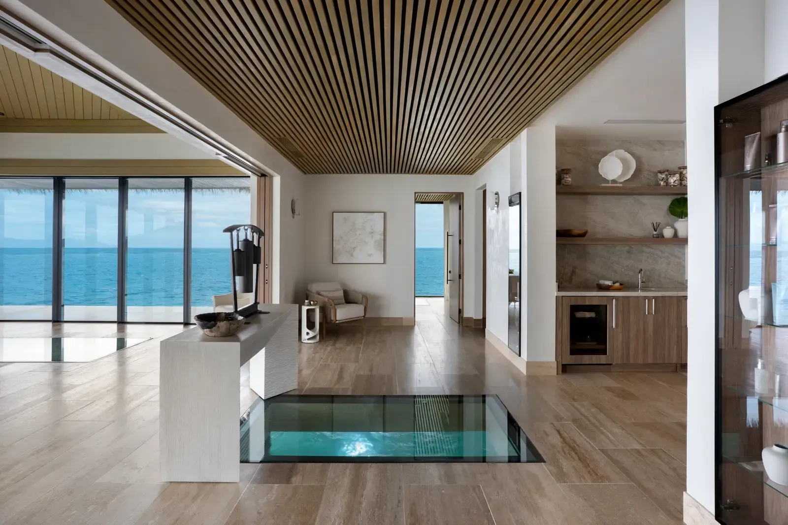 The lobby in daylight, a glass floor showing the water, glazing open to the sea