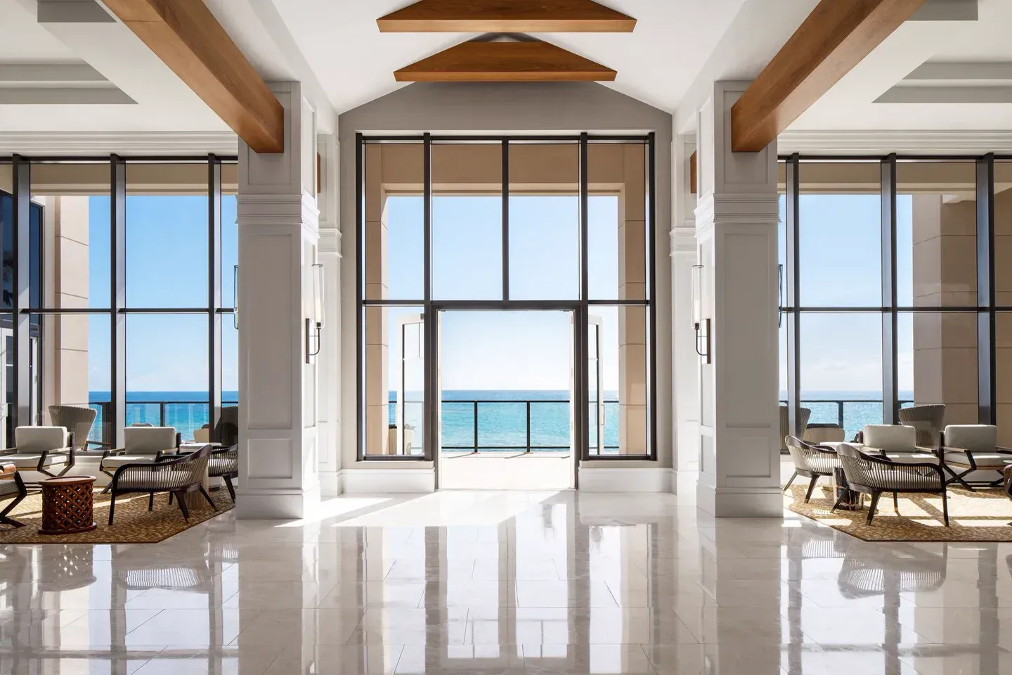 The lobby: white columns and timber beams, tall glazing open to the sea