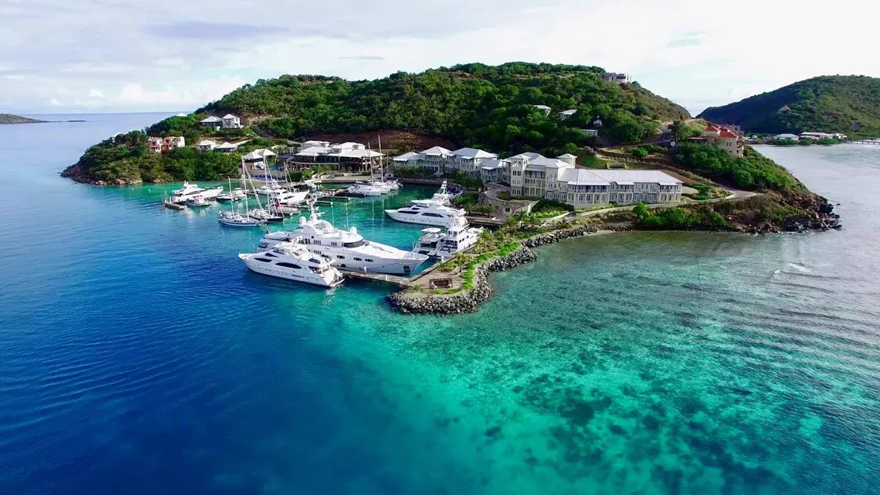 The marina on the lee of the island from the air, yachts at the docks, the resort behind and the hill above