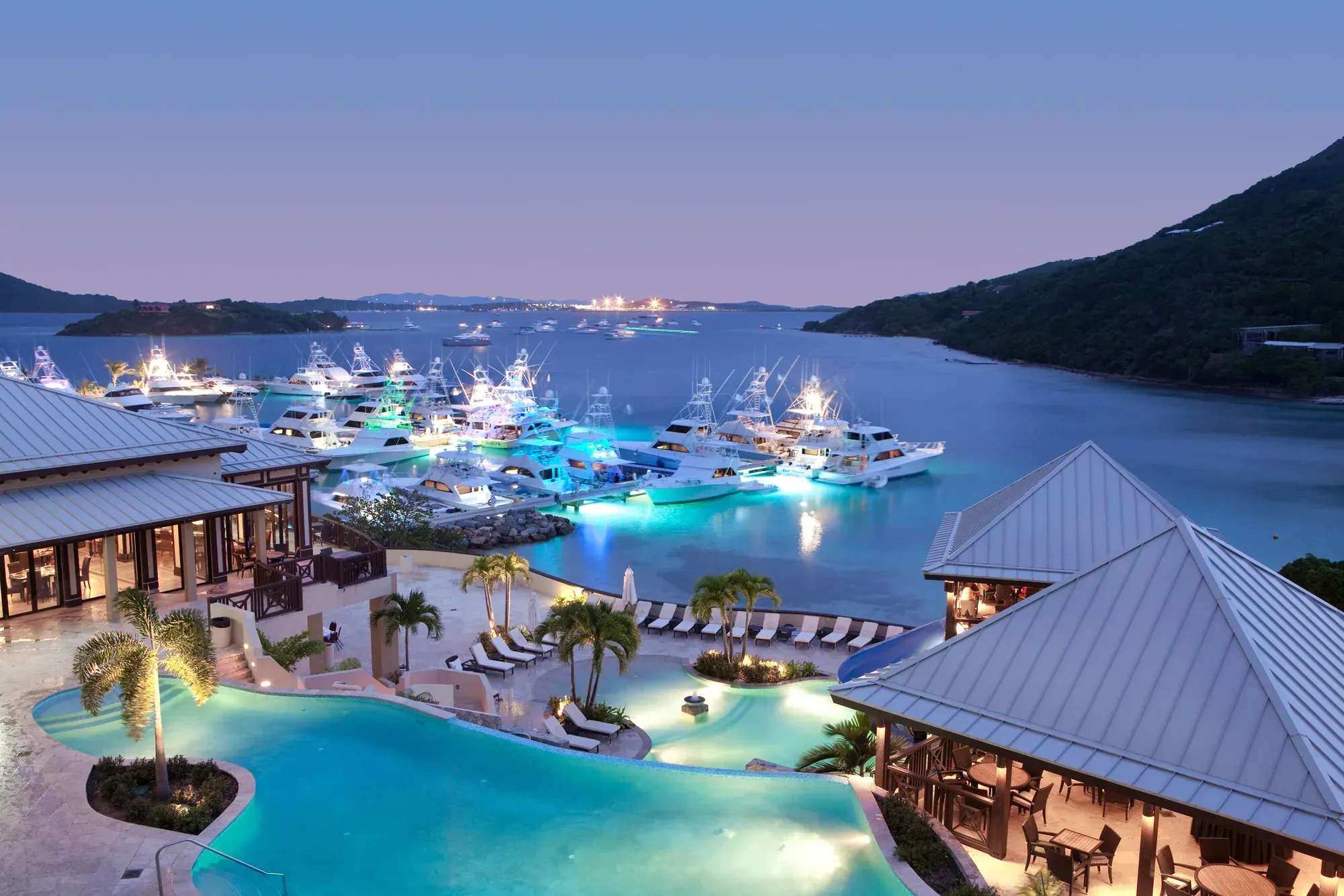The pool and pavilions at dusk, the marina lit below, the channel and Tortola beyond