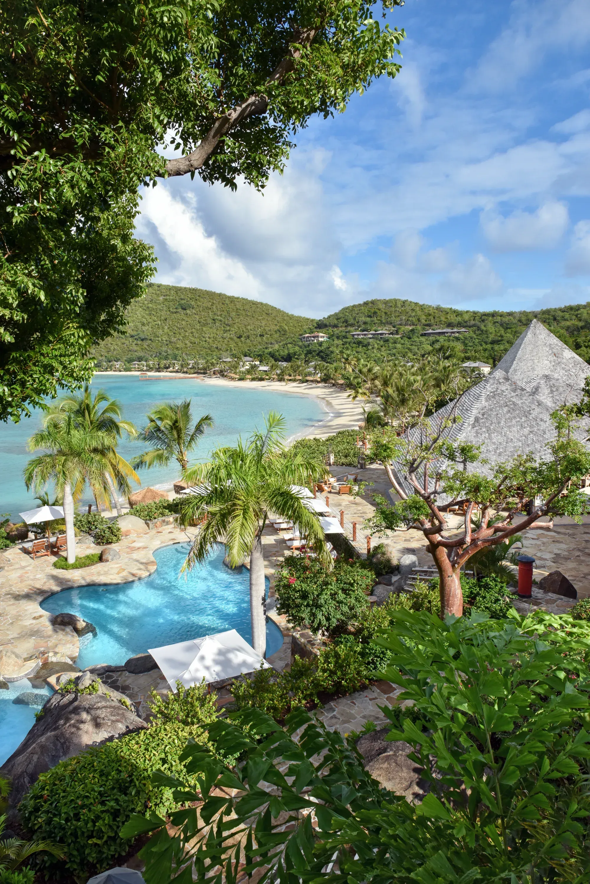 The pool and a pyramid roof from above a tree, the bay curving beyond