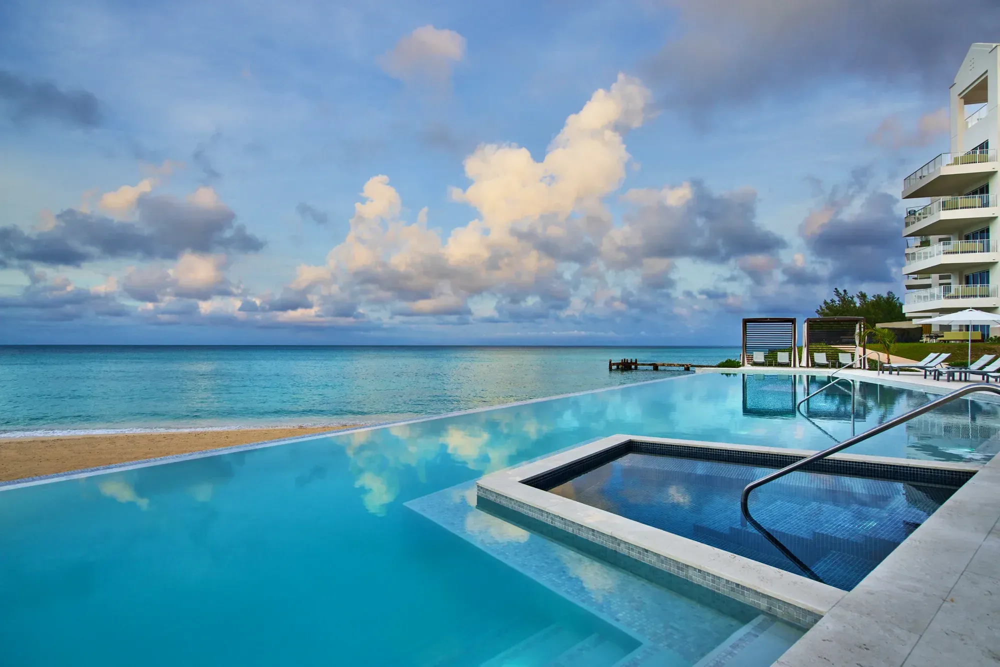An infinity pool at the edge of the beach, the sky reflected in it