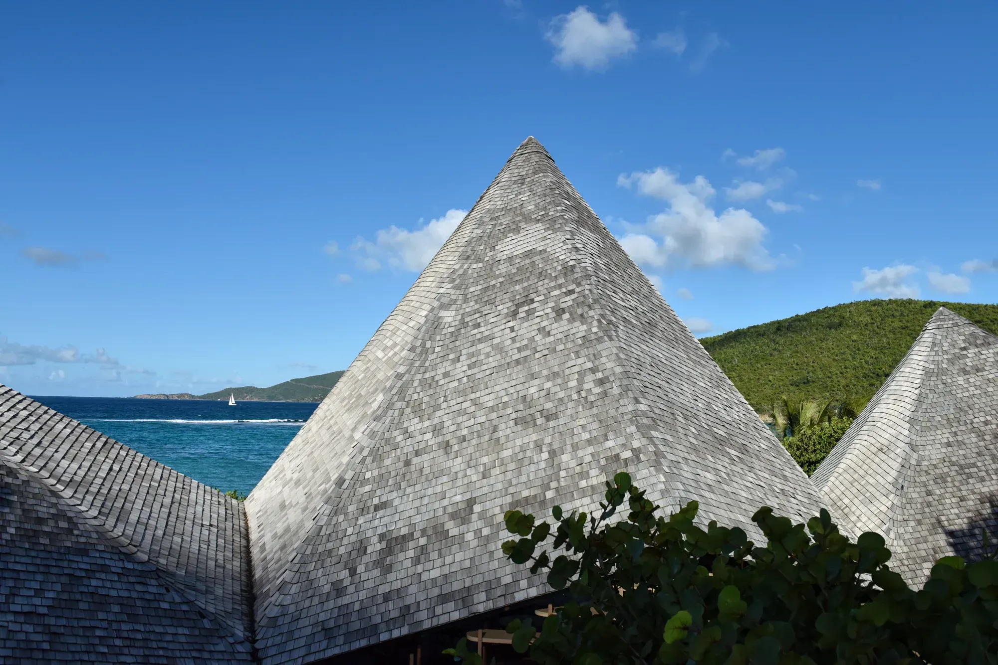 The shingled pyramid roofs against the sky, the bay and a sail beyond