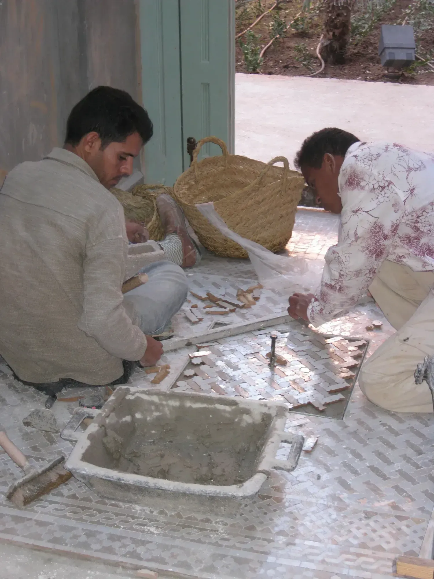 Two artisans on site setting zellige face-down on the floor