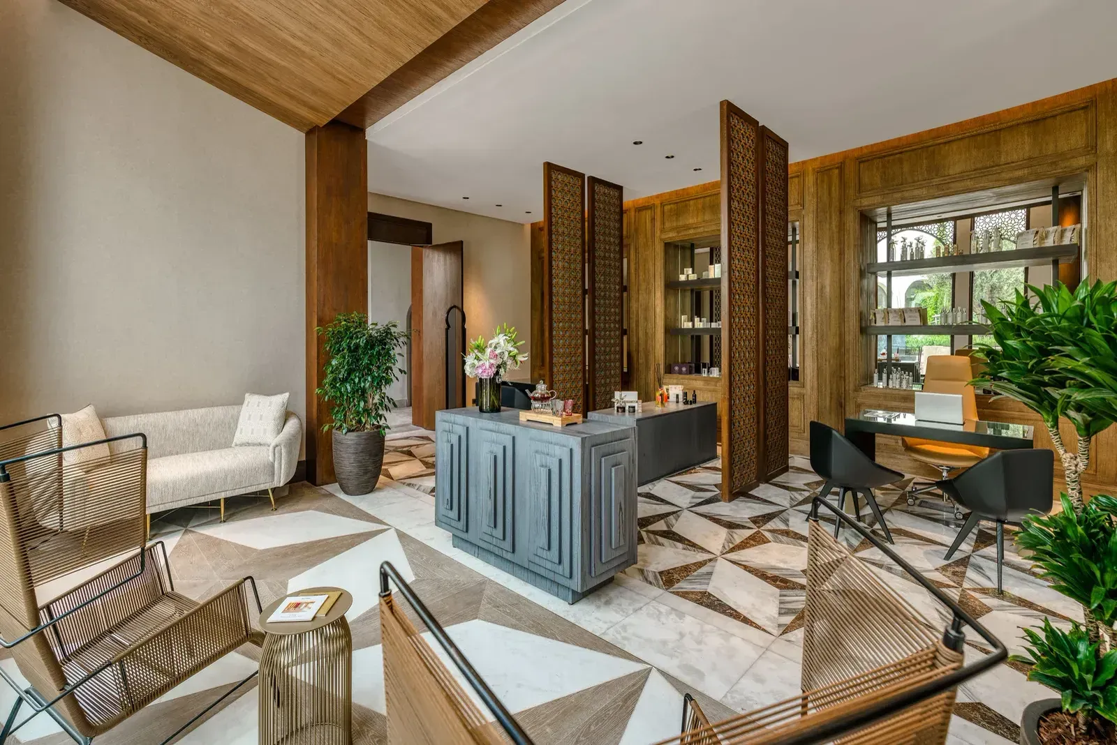 The spa reception: a grey counter on a geometric marble floor, timber screens, cane chairs