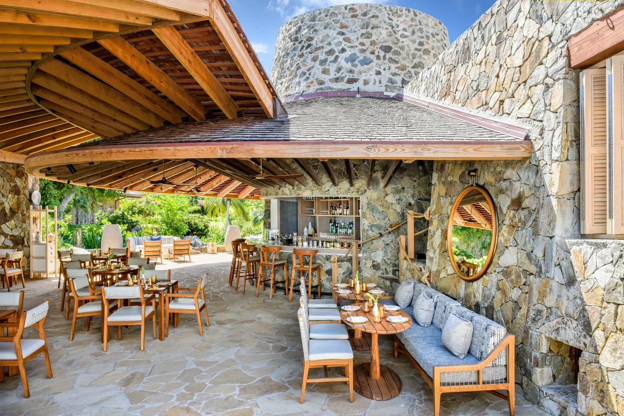 A bar under a timber roof, stone walls and a round mirror, tables set for lunch