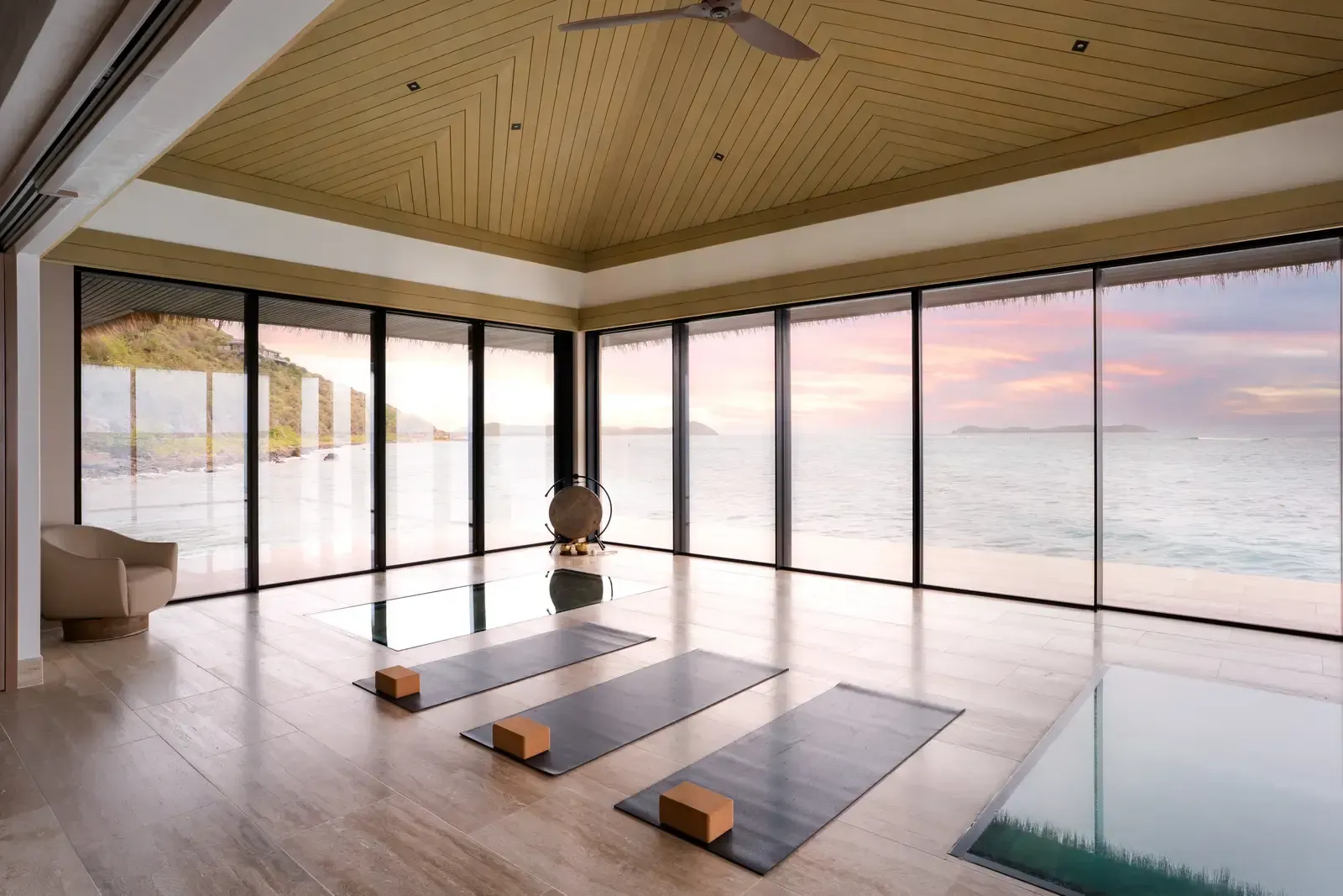 The studio at dusk: three yoga mats, glass walls on every side, the sky pink over the sea