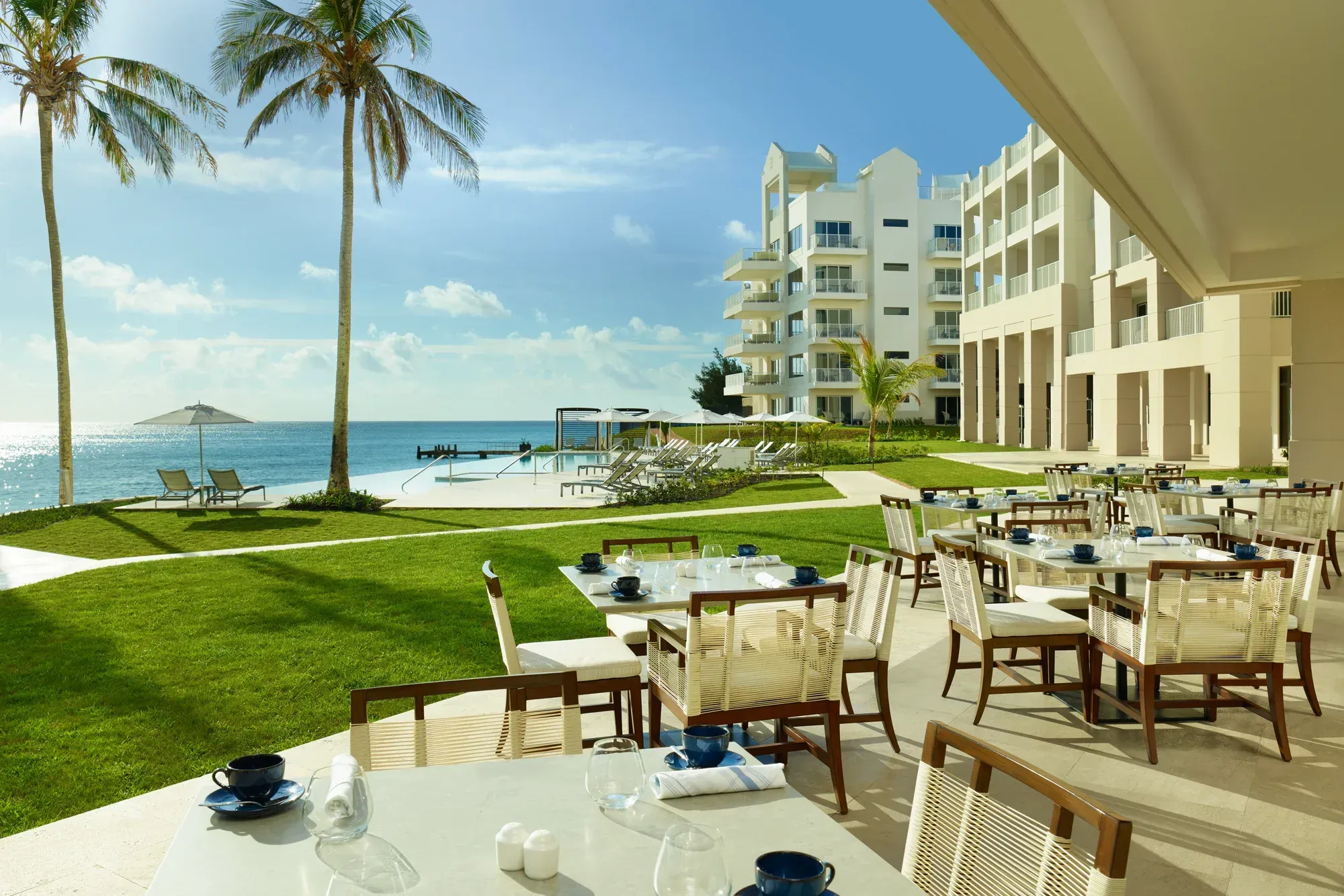 A dining terrace set for breakfast, palms and the pool beyond