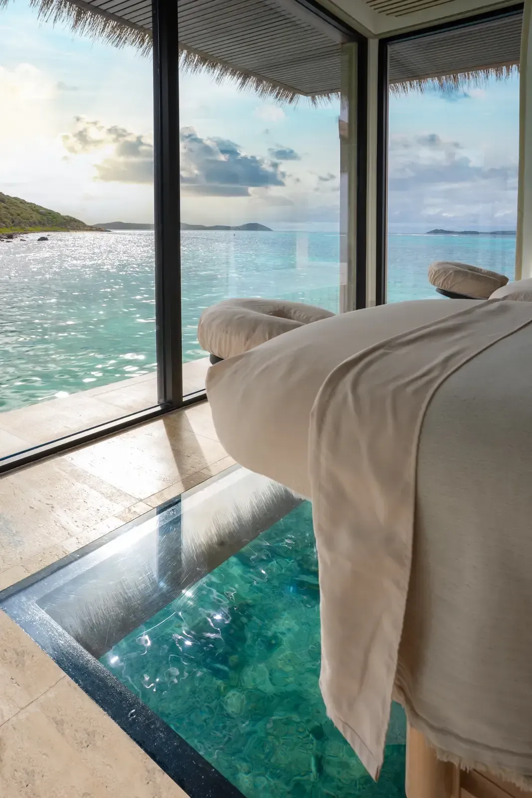 A treatment bed over a glass floor, the sea and a headland through the glass corner