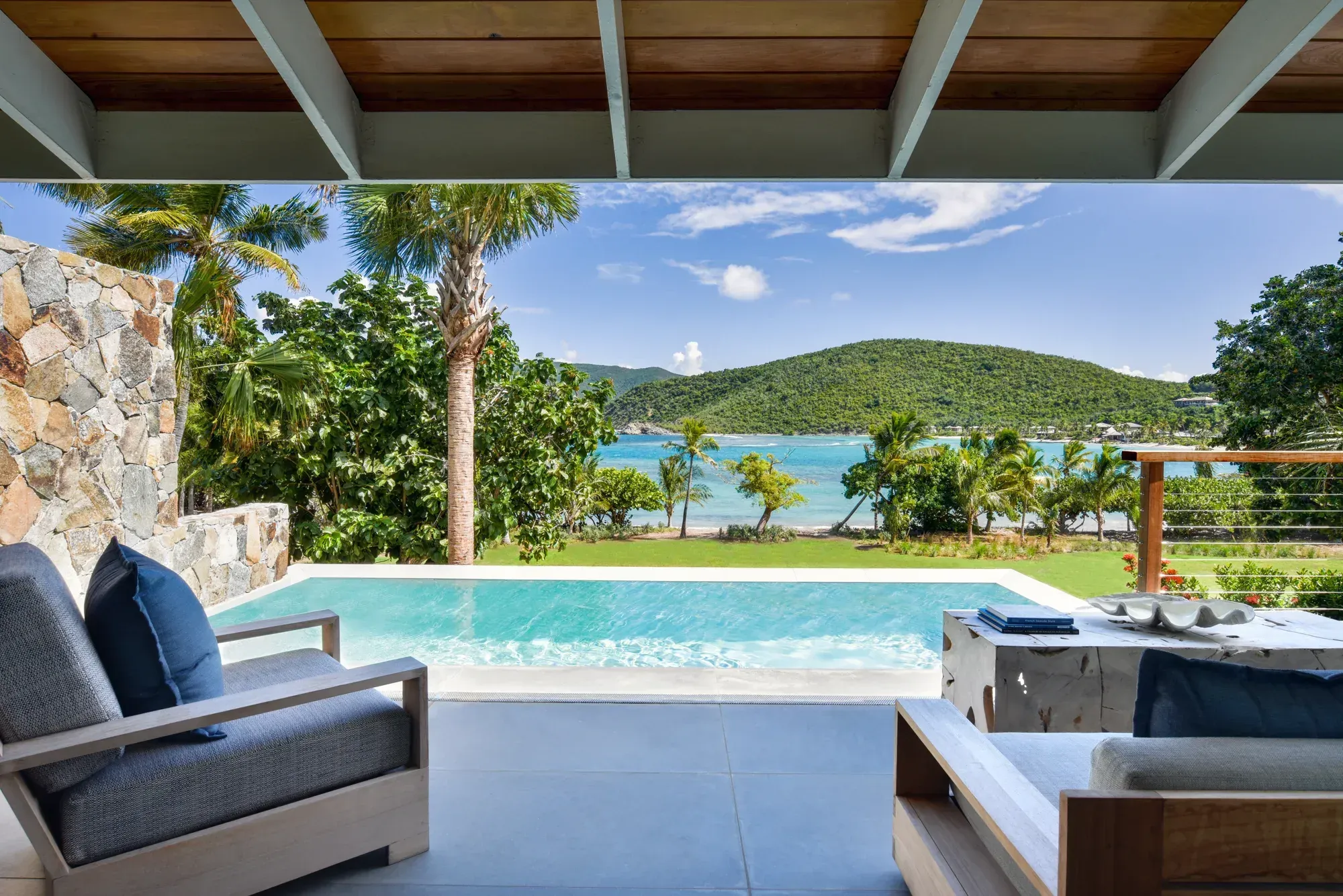 A villa terrace: a stone wall, a plunge pool and the bay through the palms