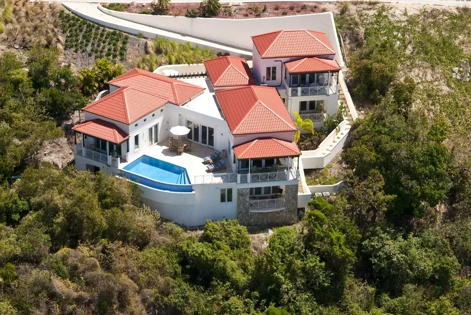 A hillside villa from the air, red tiled roofs around a pool, the scrub around it