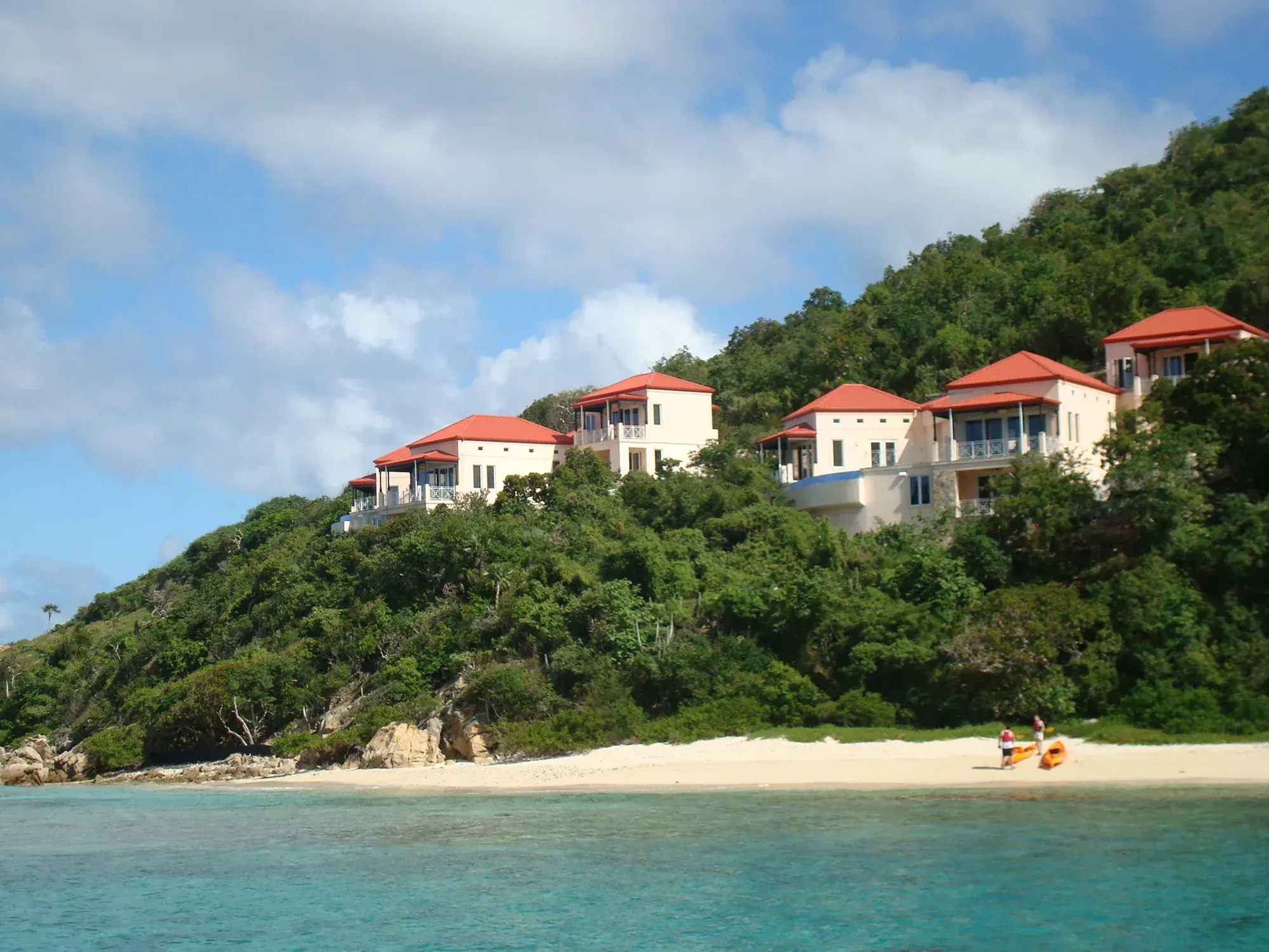 Red-roofed villas on the green hill above a small beach, seen from the water
